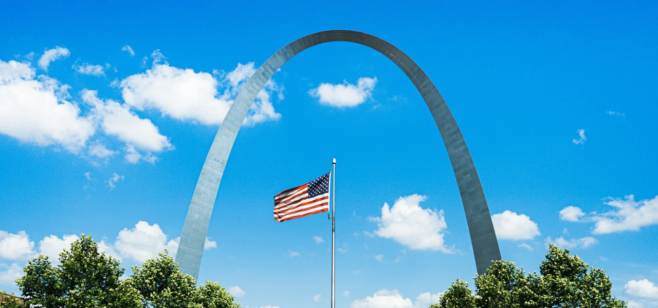 An American flag with the Gateway Arch in the background