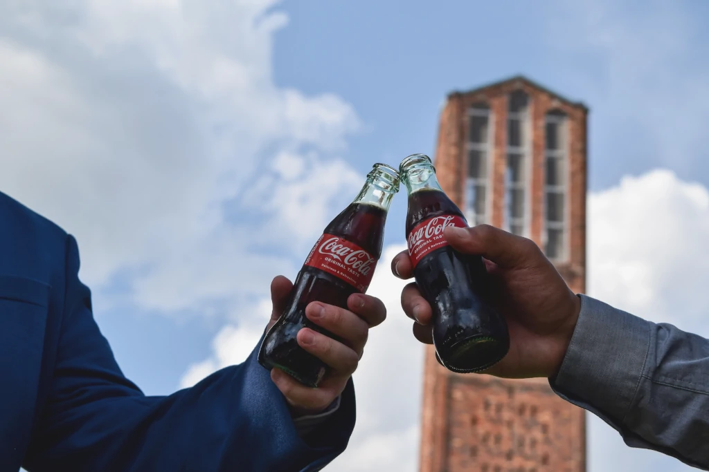 Two men in suits enjoying a bottle of coca cola each
